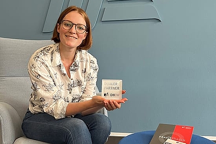 Caroline Gilberg auf einem Sessel mit dem Partnerlogo der DHBW