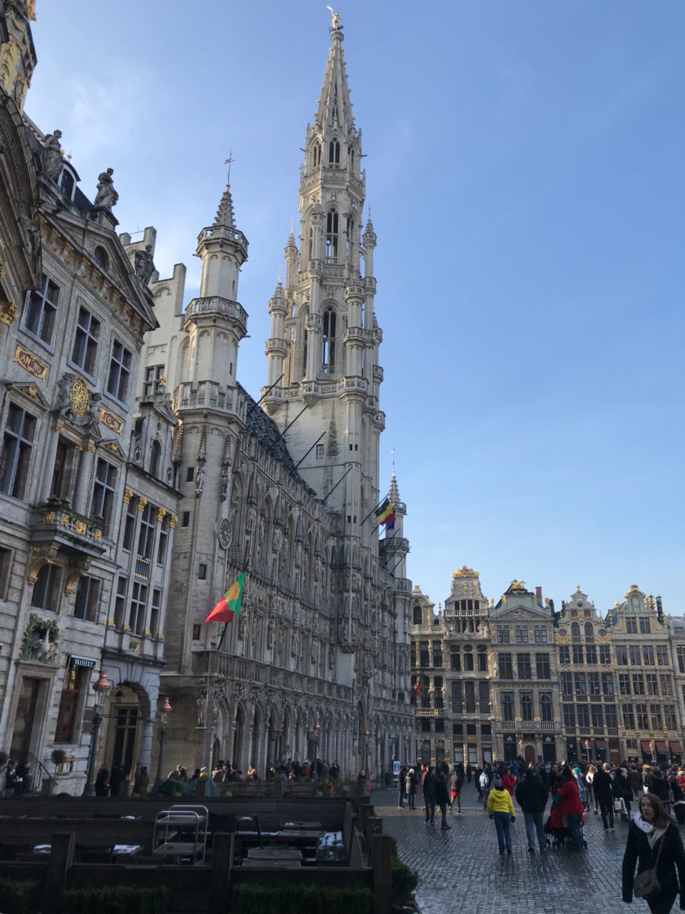 Der Grand Place in Prüssel. Es ist ein klarer blauer Himmel zu sehen und Menschen die sich auf dem Platz tummeln.