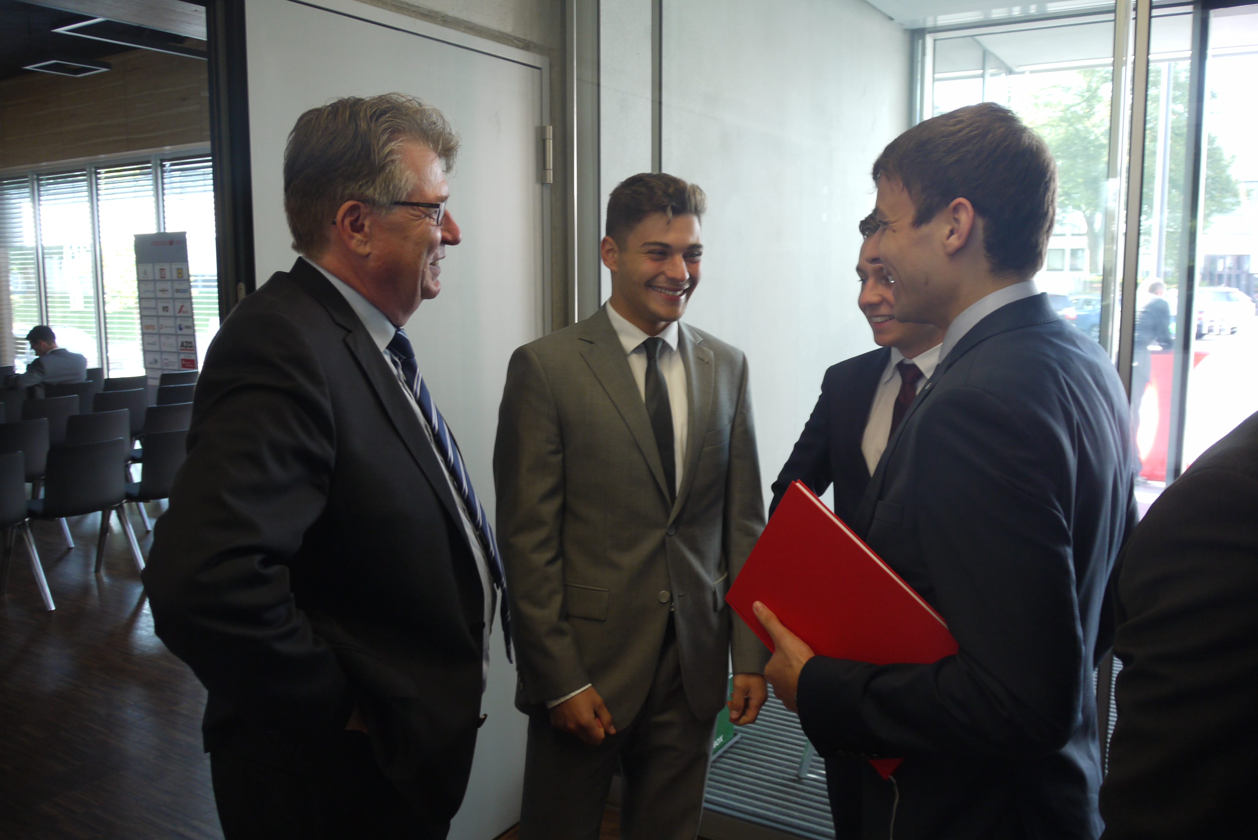 Vier Männer im Anzug stehen im Eingangsbereich des Audimax und unterhalten sich.