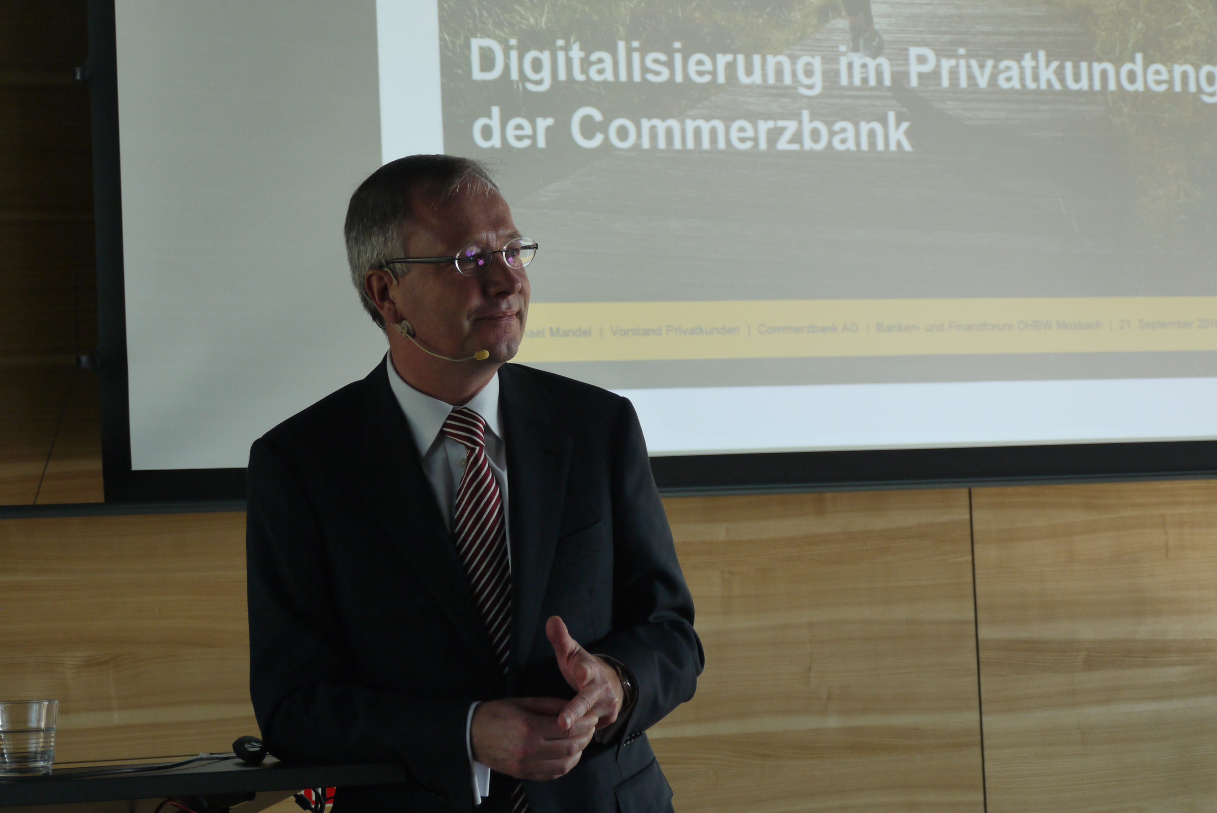 Ein älterer Mann im Anzug steht am Pult des Audimax.